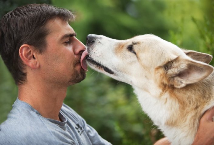 Dog kissing man on the face outdoors