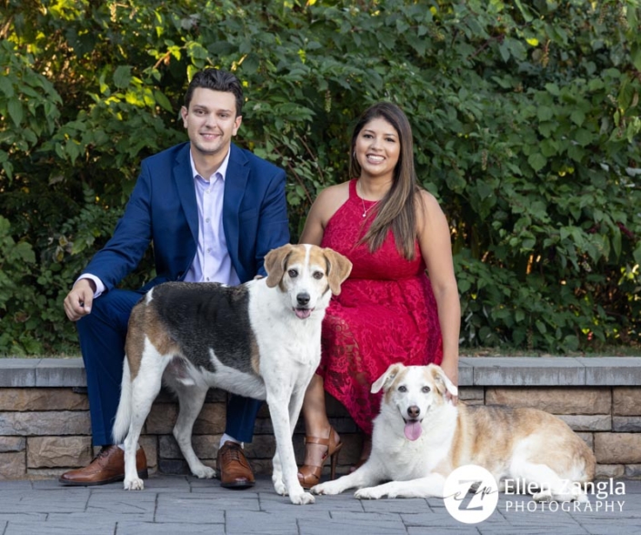 Family of two adults and two dogs sitting outside.