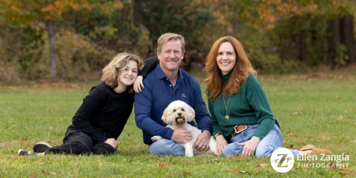 Family of three with their dog sitting outside in the fall.