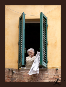 Woman in a window in Siena, Italy taking in her laundry.