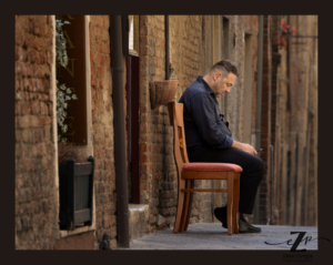 Street photo of a man sitting in alley in Tuscany.