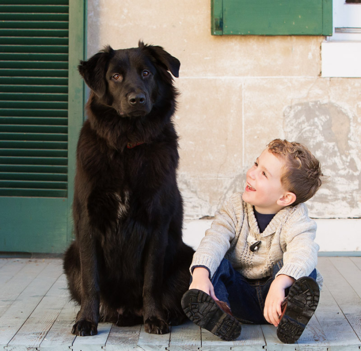 Boy sitting outside with black dog and looking at the dog laughing at Morven Park, Leesburg, VA.