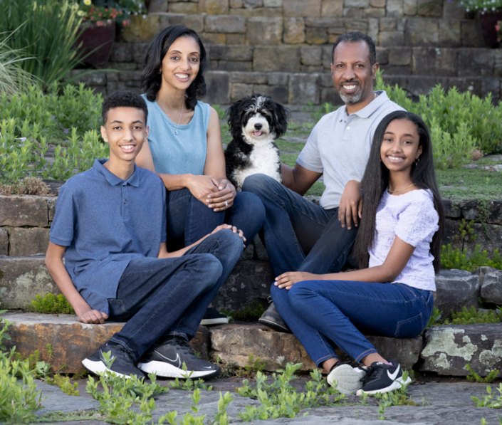 Family of four sitting outside on the steps with their mini Bernedoodle in Loudoun County, VA.