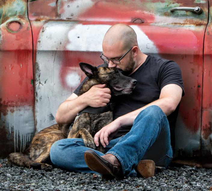 Man sit and hugging his dog while leaning against a truck in Northern VA.