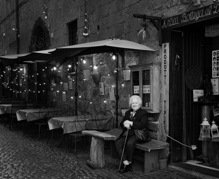 Old woman sitting outside a cafe in Tuscany, Italy.