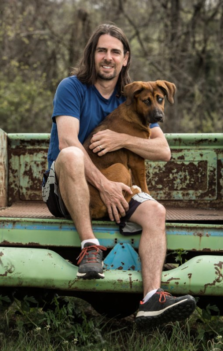 Man sitting outside on truck bed holding mixed breed puppy.